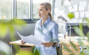 Frau steht mit Plänen in der Hand in einem modernen Büro voller Pflanzen